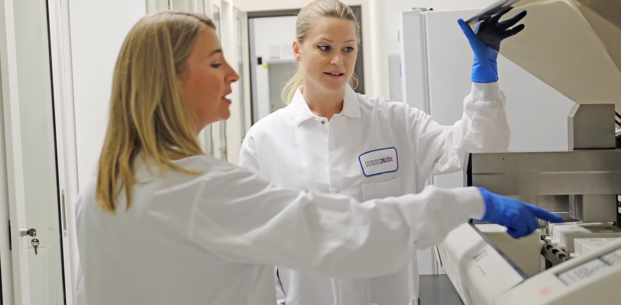 PathXdx technologists in lab coats and gloves collaborating at laboratory instrumentation
